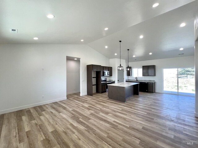 kitchen with dark brown cabinets, open floor plan, lofted ceiling, appliances with stainless steel finishes, and a kitchen island