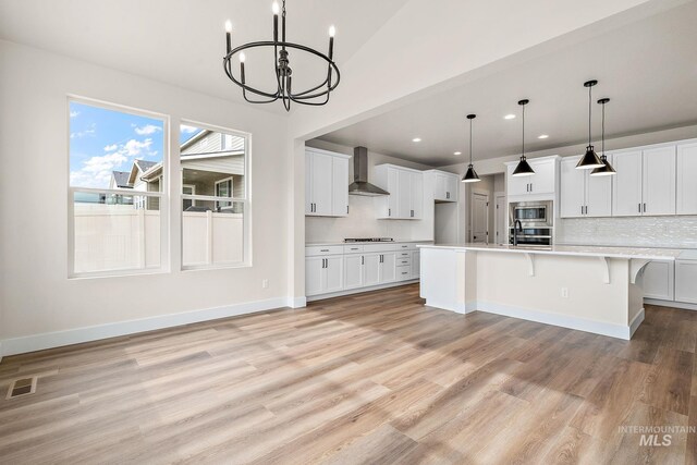 6117 N Torva Ave, Meridian, ID 83646 - kitchen featuring wall chimney range hood, light countertops, a chandelier, appliances with stainless steel finishes, and light wood finished floors