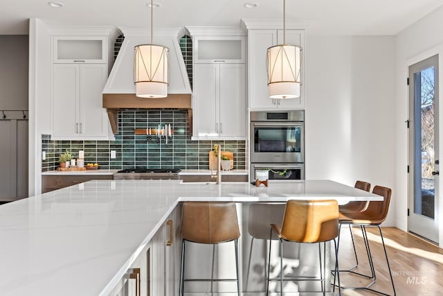 kitchen featuring decorative backsplash, stainless steel double oven, pendant lighting, and custom exhaust hood