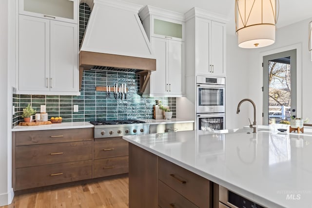 kitchen featuring white cabinetry, light countertops, appliances with stainless steel finishes, decorative backsplash, and custom range hood