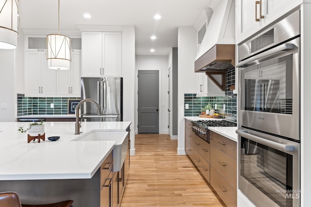 kitchen featuring light countertops, appliances with stainless steel finishes, custom exhaust hood, and light wood-style flooring