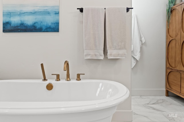 full bath featuring marble finish floor, a soaking tub, and baseboards