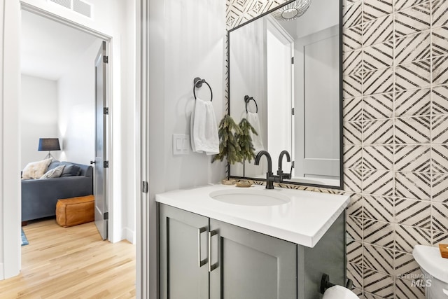 ensuite bathroom with connected bathroom, visible vents, wood finished floors, and vanity