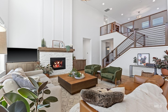 living area with visible vents, stairway, a high ceiling, a stone fireplace, and wood finished floors