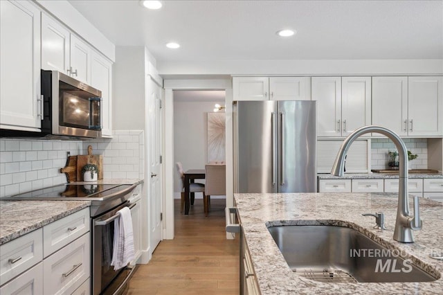 5322 N Papago Pl, Boise, ID 83713 - kitchen with stainless steel appliances, white cabinets, light wood-style floors, decorative backsplash, and light stone counters