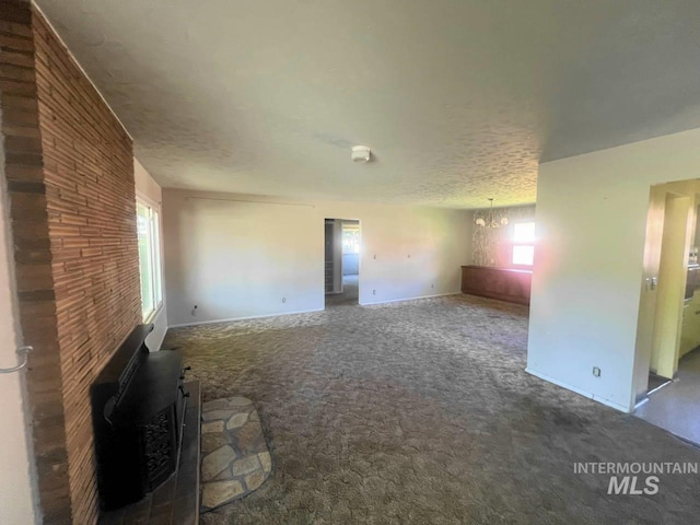 unfurnished living room with a notable chandelier, a healthy amount of sunlight, a textured ceiling, and dark carpet