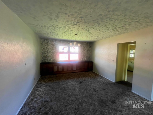 carpeted spare room with a textured ceiling and a chandelier