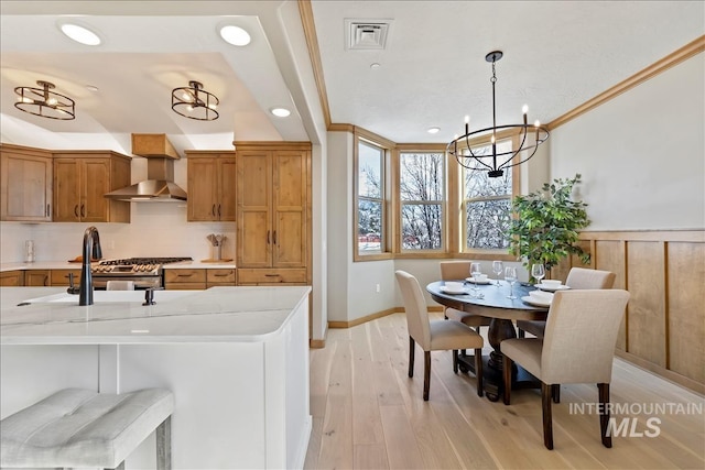 79 E Aikens Rd, Apt Eagle, ID 83616 - kitchen with wall chimney range hood, brown cabinetry, light countertops, a chandelier, and wainscoting