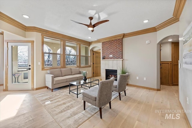 79 E Aikens Rd, Apt Eagle, ID 83616 - living room featuring arched walkways, ornamental molding, a ceiling fan, light wood-type flooring, and a tiled fireplace