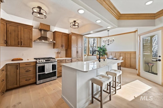 79 E Aikens Rd, Apt Eagle, ID 83616 - kitchen with range with two ovens, crown molding, brown cabinetry, wall chimney range hood, and a kitchen breakfast bar