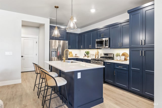 kitchen featuring sink, blue cabinetry, appliances with stainless steel finishes, a kitchen island with sink, and a kitchen breakfast bar