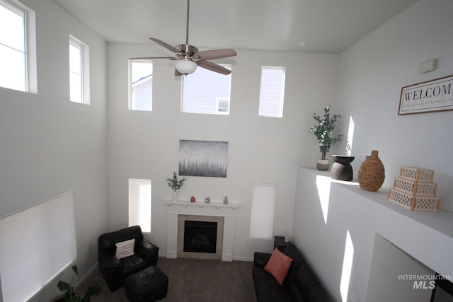 carpeted living area with a towering ceiling, a fireplace, baseboards, and a ceiling fan