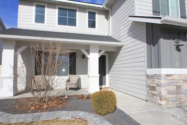 view of exterior entry featuring a porch, stone siding, and a shingled roof