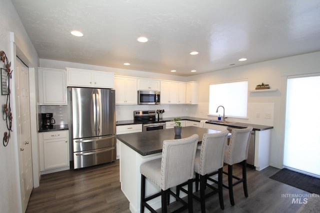 kitchen with stainless steel appliances, dark wood-style flooring, dark countertops, and a center island