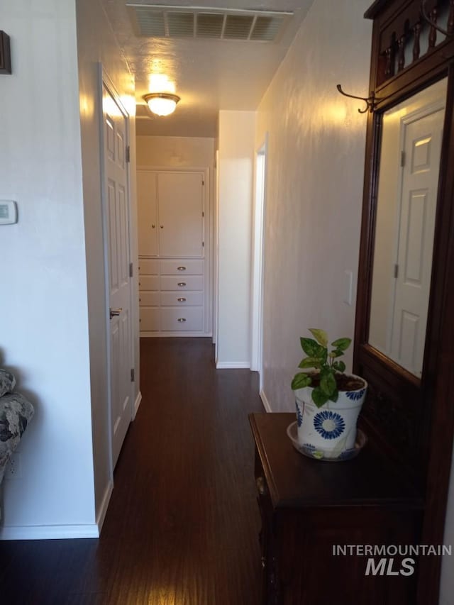 hallway with visible vents, dark wood-type flooring, and baseboards