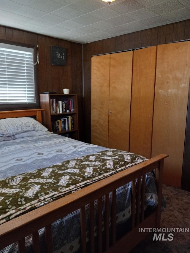 carpeted bedroom featuring a closet and wooden walls