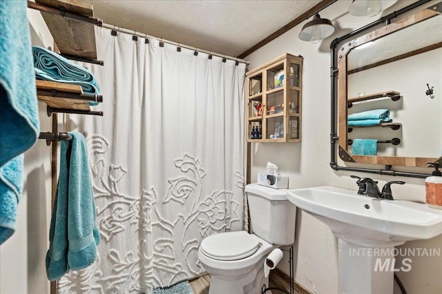 bathroom with crown molding, curtained shower, toilet, a sink, and a textured ceiling