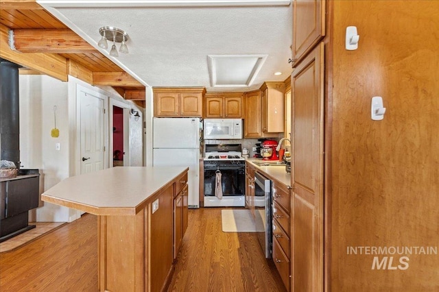 kitchen with light wood finished floors, white appliances, a center island, light countertops, and a sink