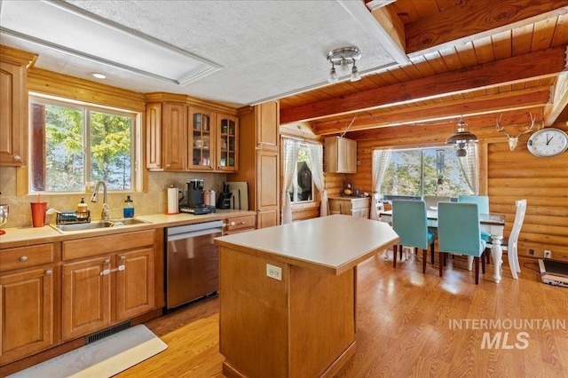 kitchen with a sink, light countertops, a center island, dishwasher, and glass insert cabinets