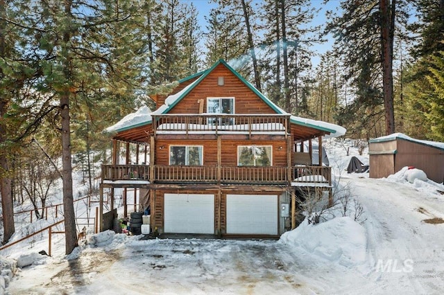 snow covered house featuring a garage, a balcony, and faux log siding