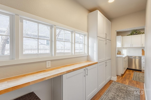 kitchen with light wood-type flooring, butcher block countertops, stainless steel dishwasher, white cabinetry, and decorative backsplash