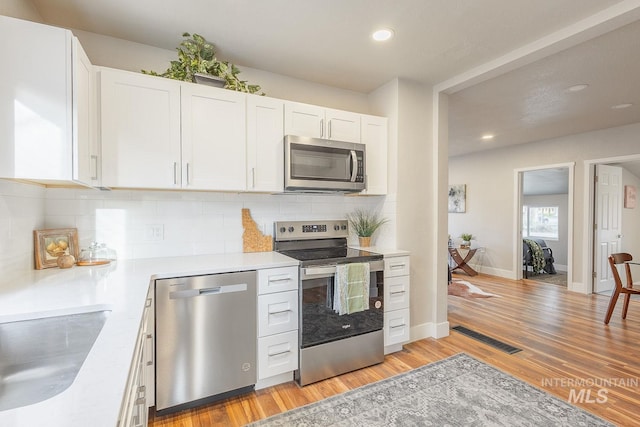 kitchen featuring visible vents, light countertops, light wood-type flooring, decorative backsplash, and appliances with stainless steel finishes