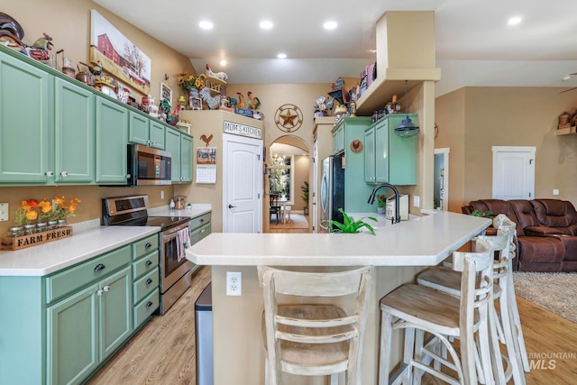 kitchen featuring appliances with stainless steel finishes, light hardwood / wood-style flooring, green cabinets, and kitchen peninsula