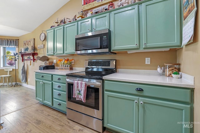 kitchen featuring light hardwood / wood-style floors, appliances with stainless steel finishes, vaulted ceiling, and green cabinetry