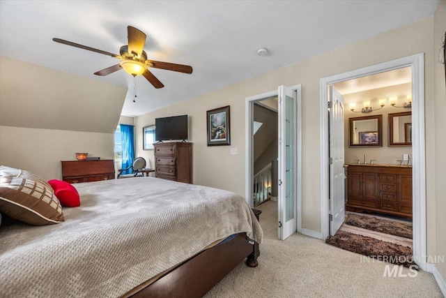 bedroom featuring a ceiling fan, light colored carpet, vaulted ceiling, baseboards, and ensuite bath