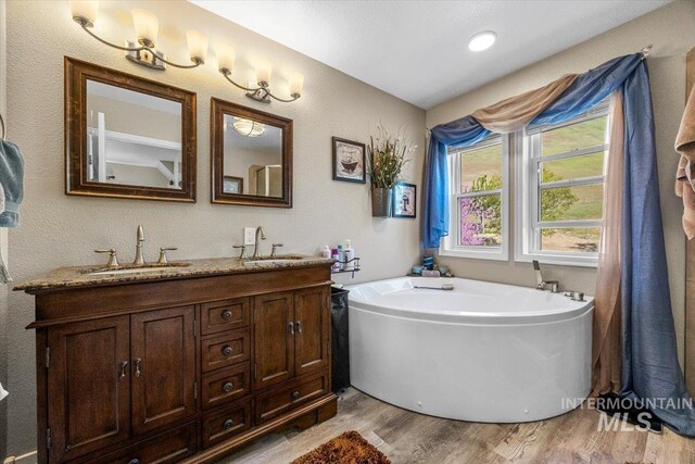 full bath with double vanity, a sink, a bath, and wood finished floors