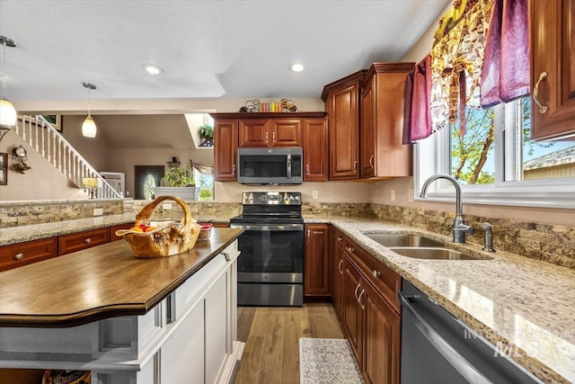 kitchen with light stone counters, a sink, light wood-style flooring, appliances with stainless steel finishes, and decorative light fixtures