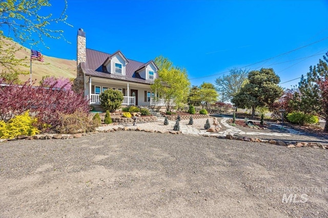 cape cod home with a chimney, a porch, and metal roof
