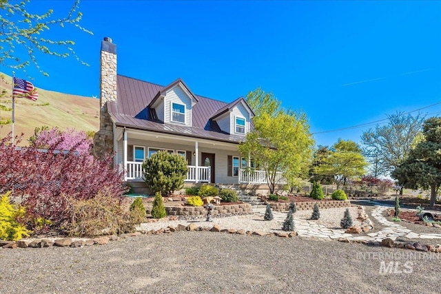 cape cod house with covered porch, a standing seam roof, metal roof, and a chimney