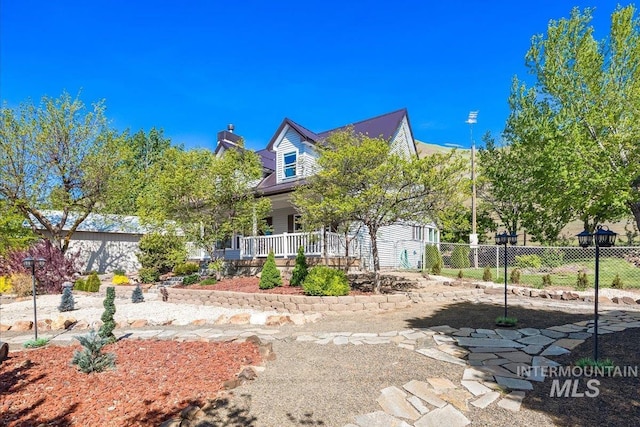 cape cod home featuring a porch, fence, and a chimney