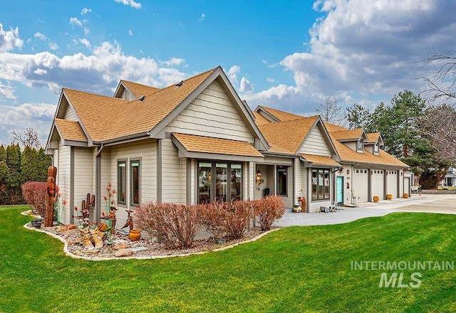 rear view of property featuring a garage, a lawn, roof with shingles, and concrete driveway
