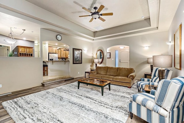 living area featuring a ceiling fan, wood finished floors, arched walkways, a raised ceiling, and visible vents