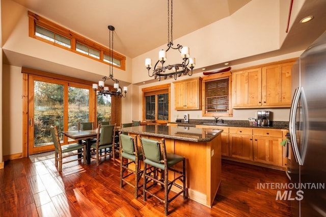 kitchen featuring an inviting chandelier, a high ceiling, a kitchen bar, stainless steel fridge, and a center island