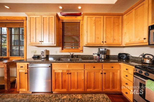 kitchen with dark wood-style flooring, appliances with stainless steel finishes, a sink, dark stone countertops, and recessed lighting