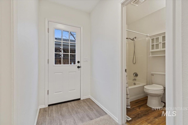 bathroom with hardwood / wood-style flooring, shower / bathtub combination, and toilet