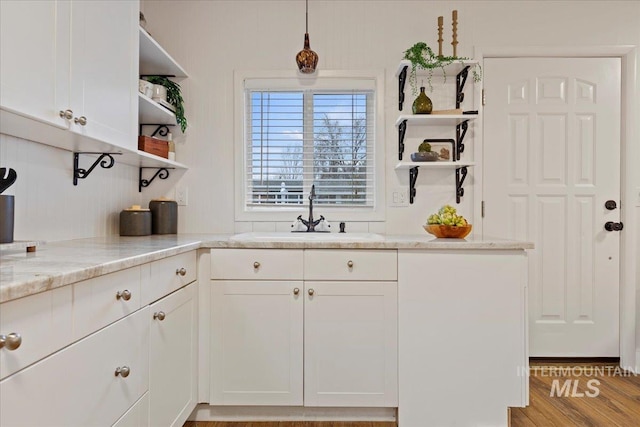 kitchen with white cabinetry, hanging light fixtures, sink, and light stone counters