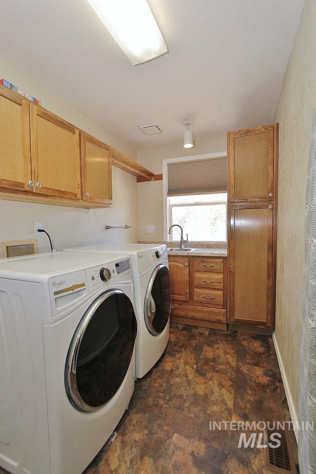 washroom featuring a textured wall, stone finish flooring, washer and clothes dryer, a sink, and cabinet space