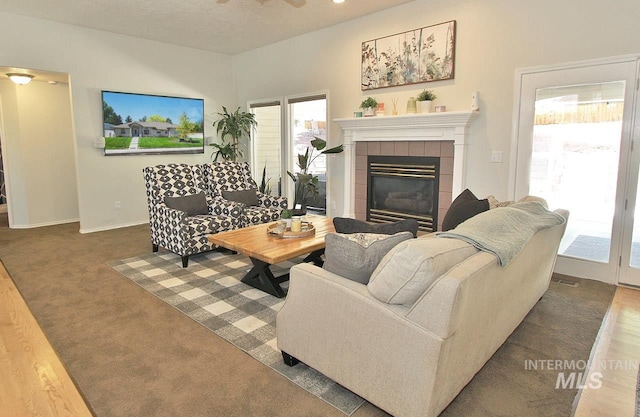living room featuring a tiled fireplace, baseboards, visible vents, and a wealth of natural light