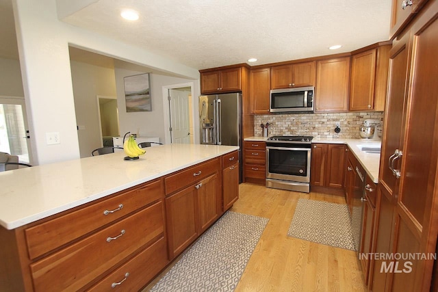 kitchen featuring light countertops, appliances with stainless steel finishes, brown cabinets, and light wood-style flooring