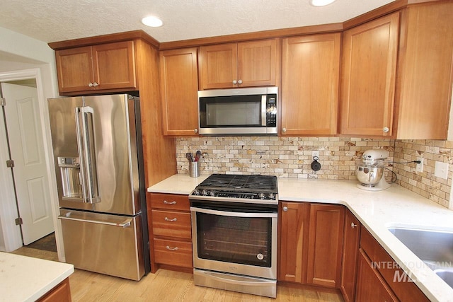 kitchen with light countertops, brown cabinets, appliances with stainless steel finishes, and decorative backsplash