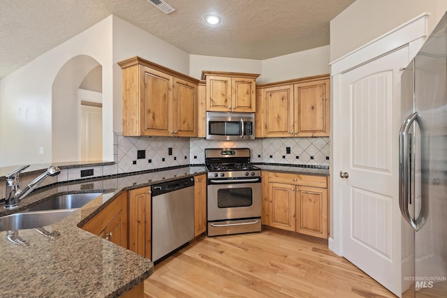 3993 N Heritage View Ave, Meridian, ID 83646 - kitchen featuring appliances with stainless steel finishes, a sink, a textured ceiling, dark stone counters, and light wood finished floors