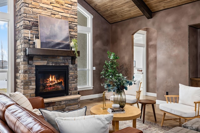 living area featuring arched walkways, beam ceiling, a fireplace, light wood-type flooring, and wooden ceiling