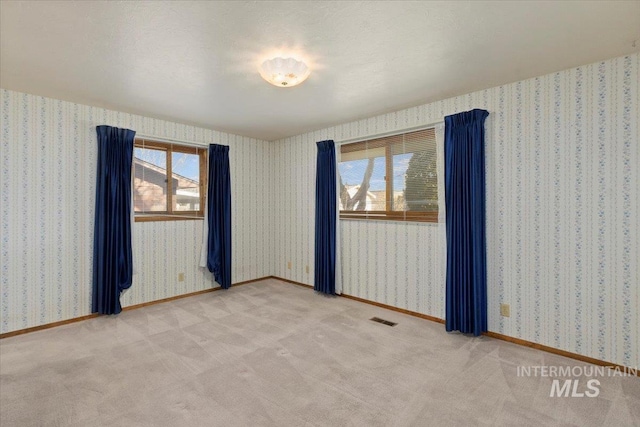 spare room with light carpet, visible vents, wallpapered walls, and baseboards