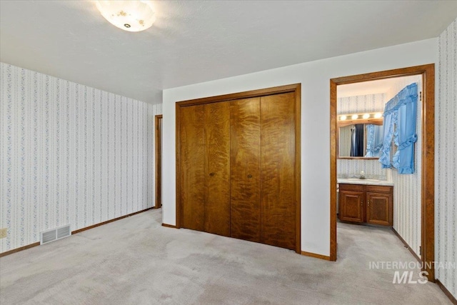 unfurnished bedroom featuring light carpet, visible vents, wallpapered walls, and a closet