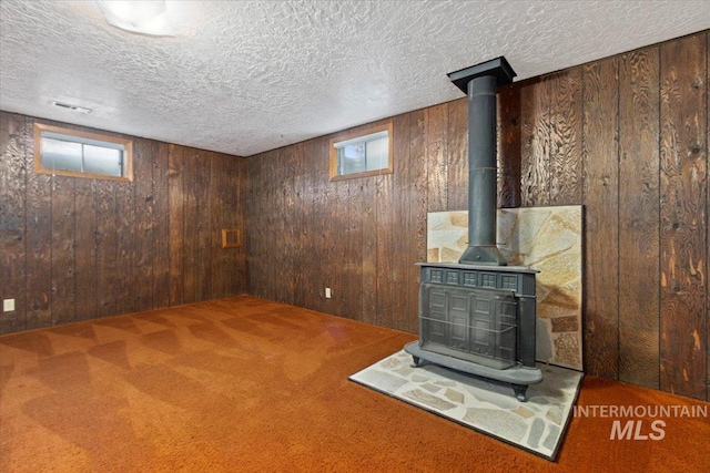 below grade area featuring carpet flooring, a wood stove, wooden walls, and a textured ceiling