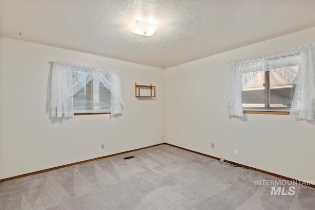 empty room with light carpet, visible vents, a textured ceiling, and baseboards